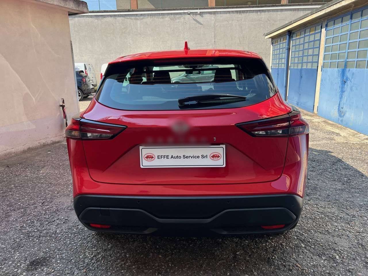 Un'auto usata rossa nel cortile coi portoni blu, con la targa di cortesia EFFE