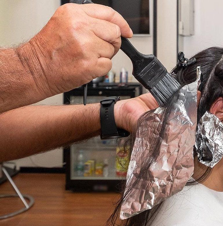 Il colore: la mano col pennello stende la tinta sulle ciocche scure, fra le cartine d'alluminio.