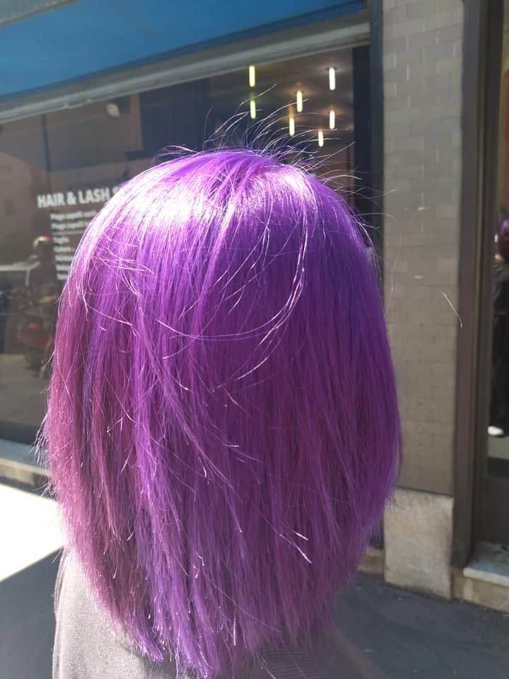 Un caschetto viola acceso, di spalle, sul marciapiede davanti alla loro vetrina con la scritta Hair & Lash.