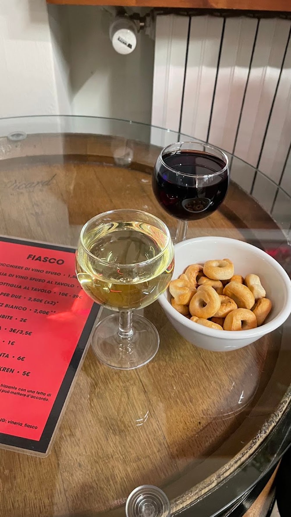 Un bicchiere di bianco e uno di rosso con una scodella di taralli, sul tavolino ricavato da una botte