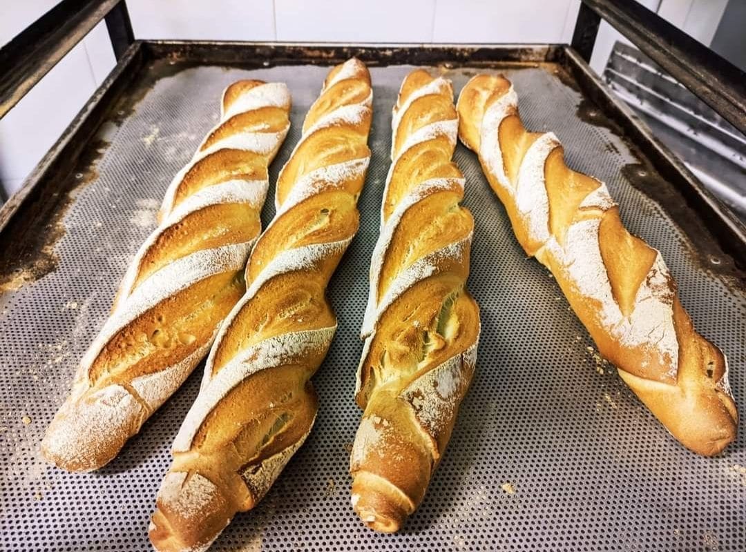 Quattro baguette dorate con i tagli, sulla teglia forata.