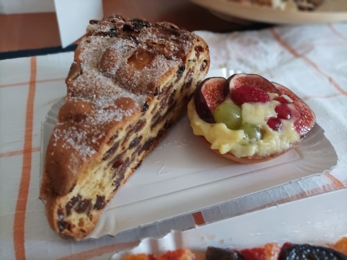 Una fetta di treccia dolce con l'uvetta e una crostatina con crema, fichi, uva e lamponi.