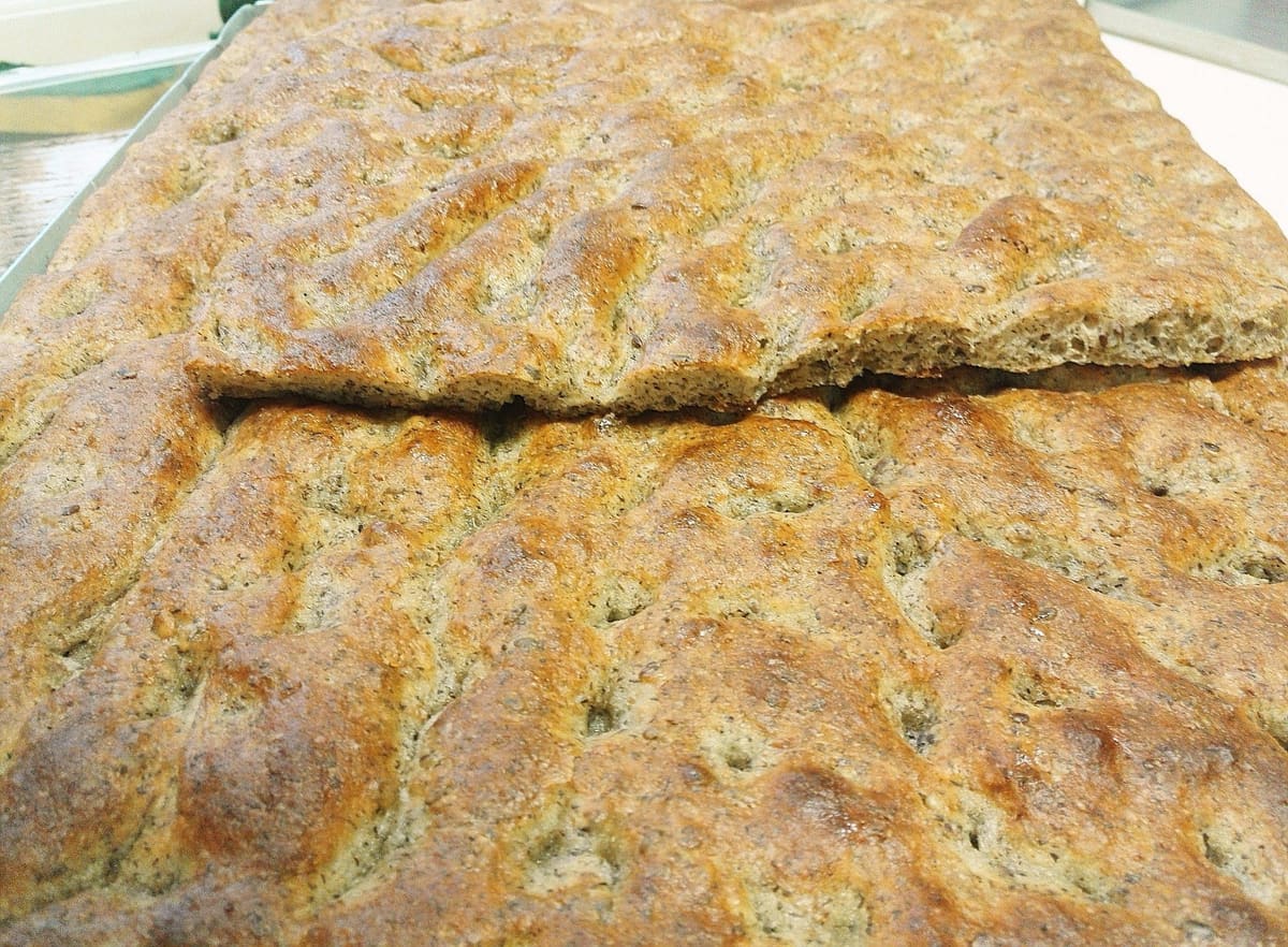 Una teglia di focaccia scura al grano saraceno e farro, tagliata.