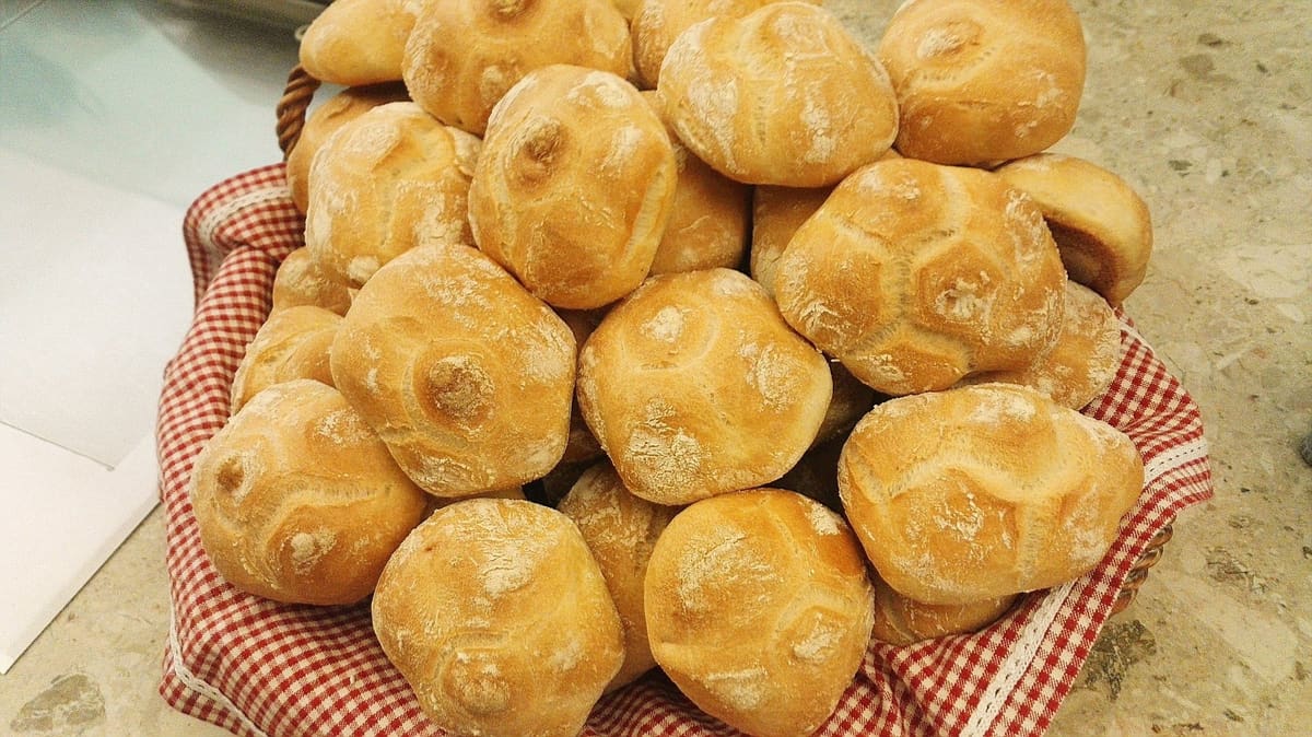Un cesto di michette dorate su un tovagliolo a quadretti rossi.