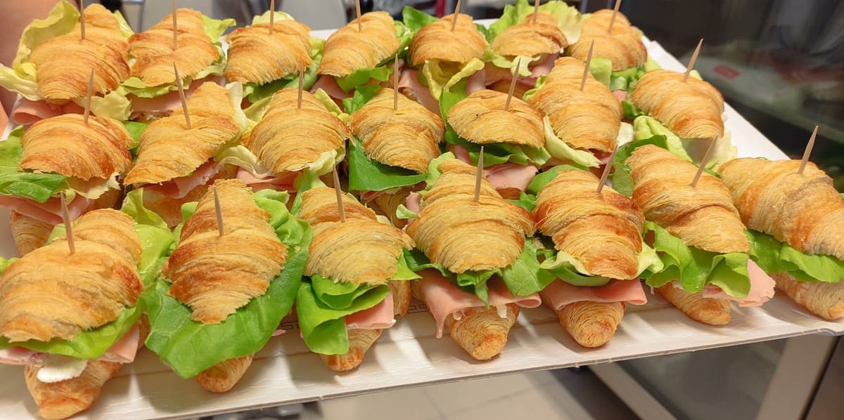 Un vassoio di mini croissant farciti con prosciutto e insalata, infilzati con uno stecchino.