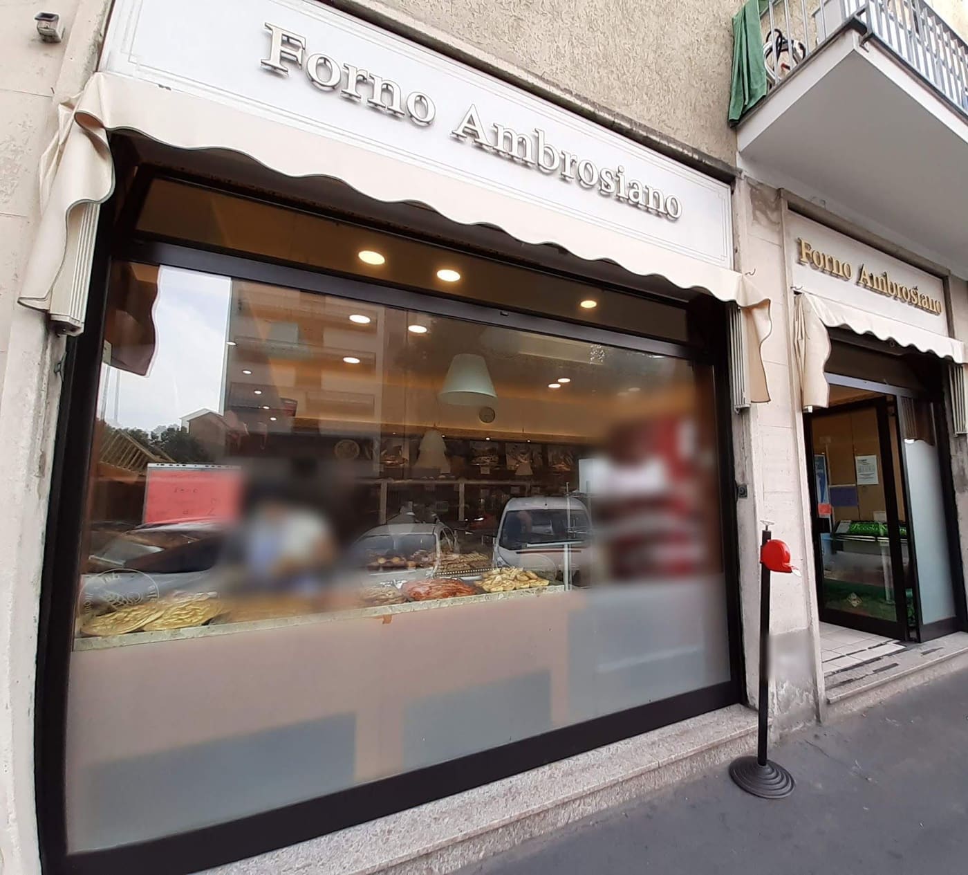 La vetrina e la porta del forno sotto le due insegne Forno Ambrosiano, con la tenda color crema.