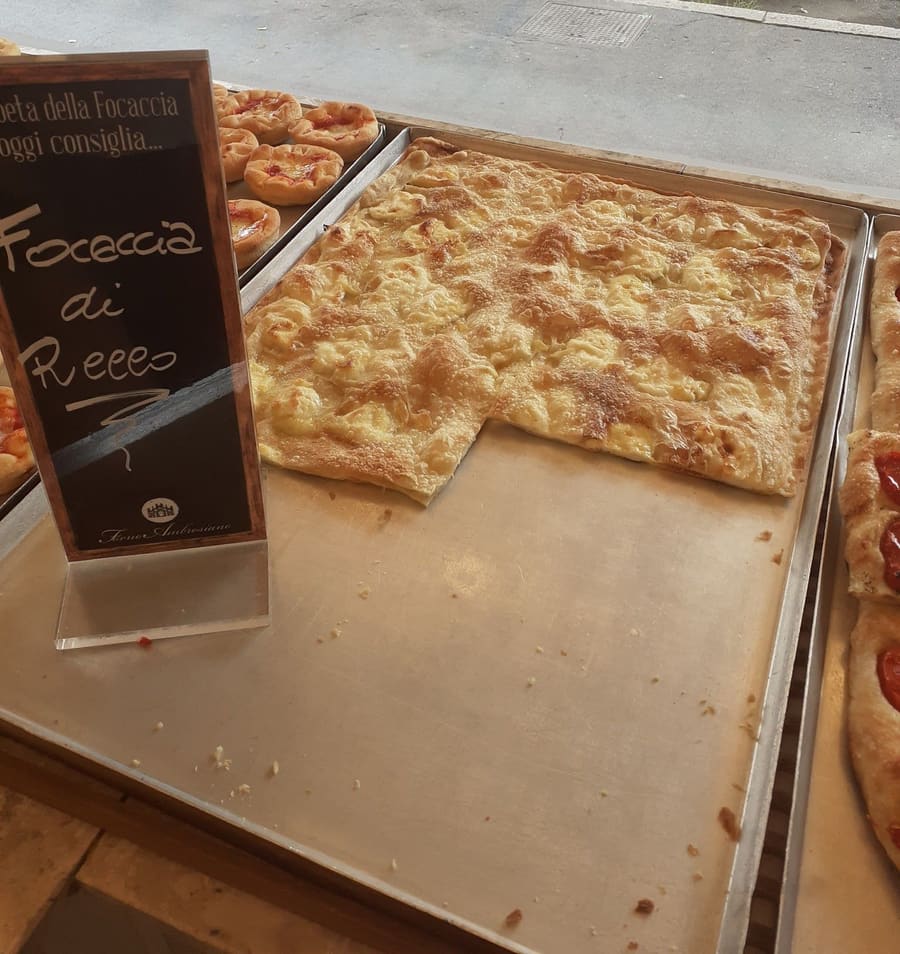 Sul banco una lavagnetta scritta a mano, Focaccia di Recco, accanto alla teglia di focaccia al formaggio.
