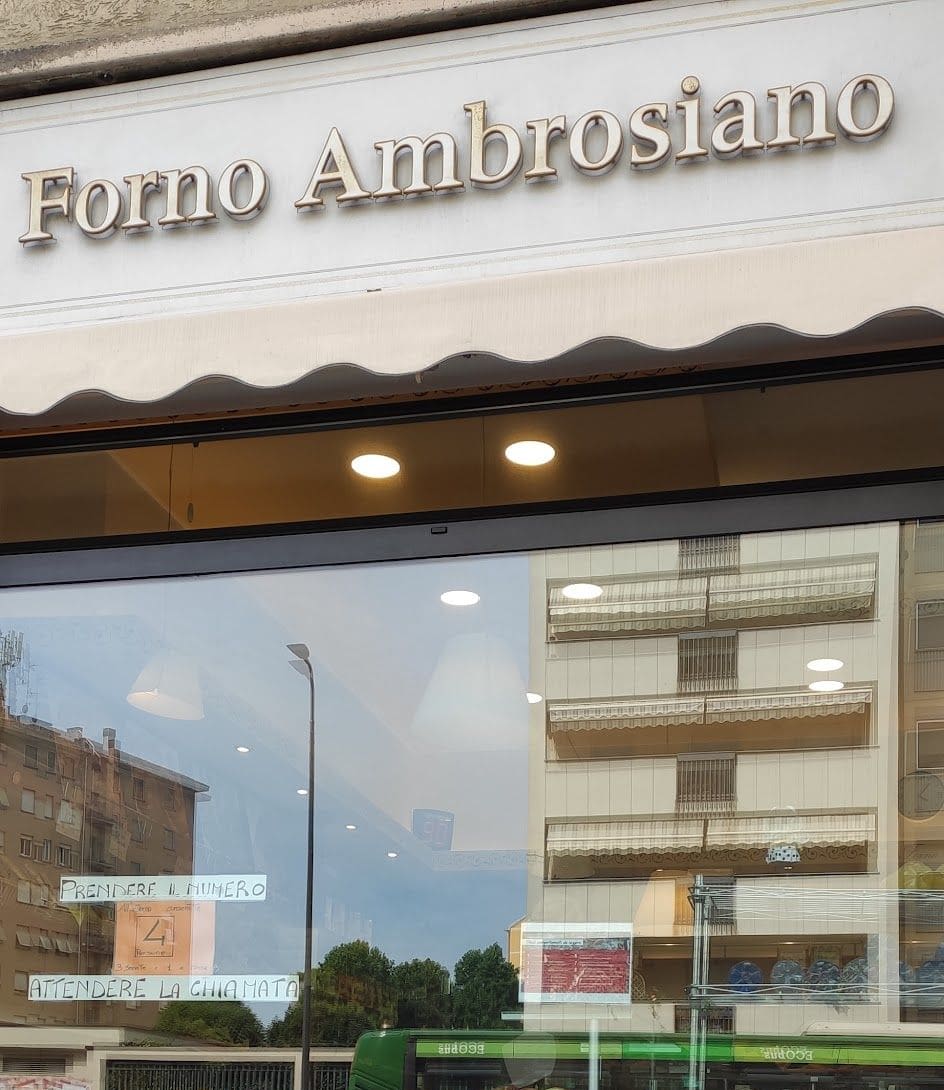 La vetrina sotto l'insegna Forno Ambrosiano, coi cartelli scritti a mano: prendere il numero, attendere la chiamata.