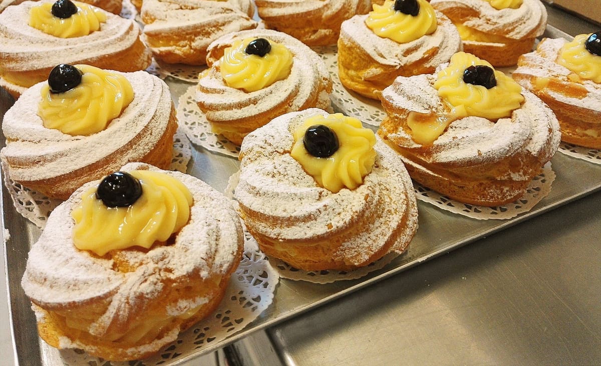 Zeppole di San Giuseppe con lo zucchero a velo, la crema gialla e un'amarena sopra.