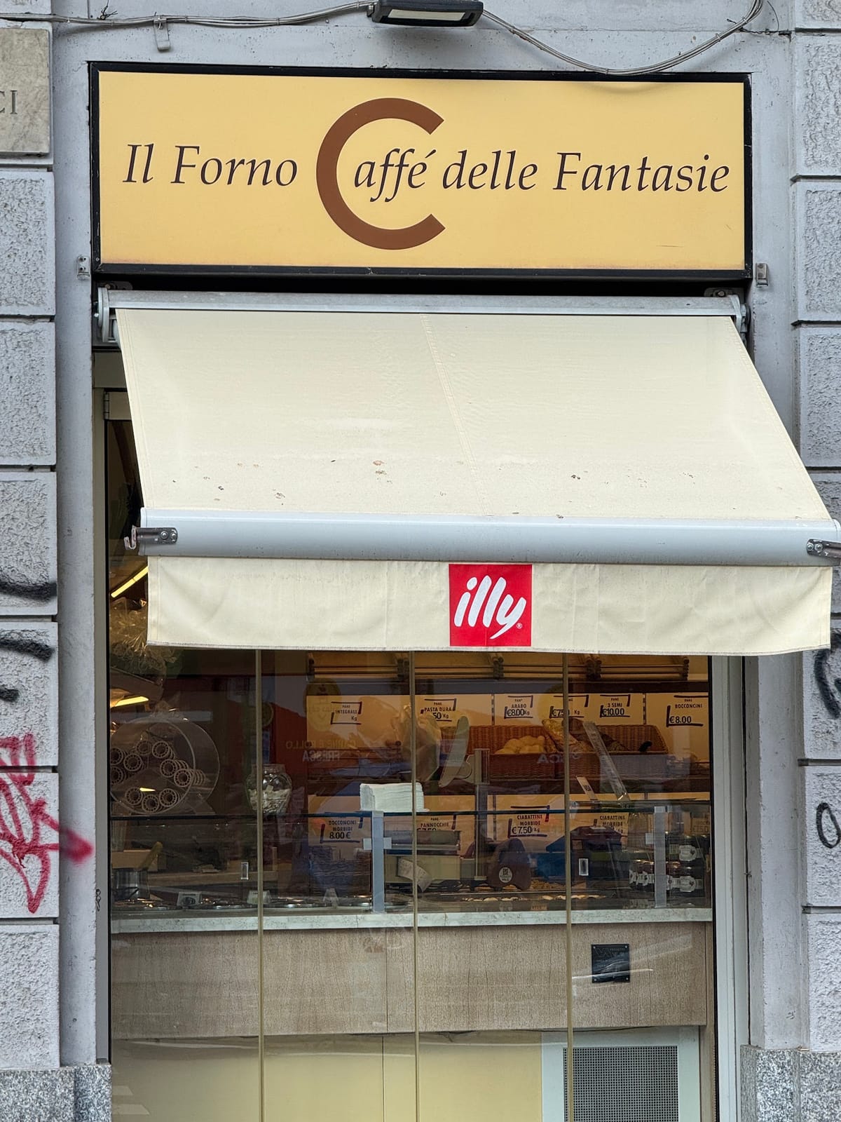 La facciata del Forno Caffè delle Fantasie: insegna crema con la grande C marrone e tenda parasole
