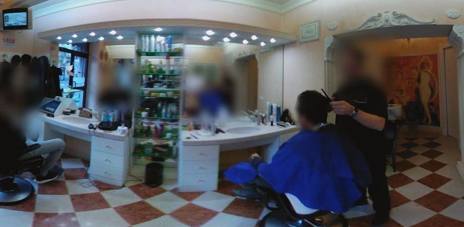 Il salone: le postazioni con gli specchi e le lucine, le mensole dei prodotti, le poltrone, il pavimento a scacchiera; in fondo, oltre l'arco, l'affresco.