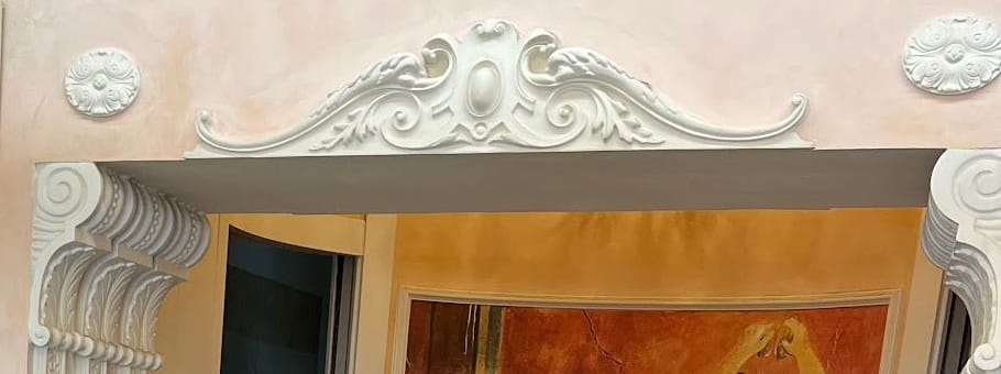 L'arco con le mensole a volute e il cartiglio in stucco; sotto, la cima dell'affresco.