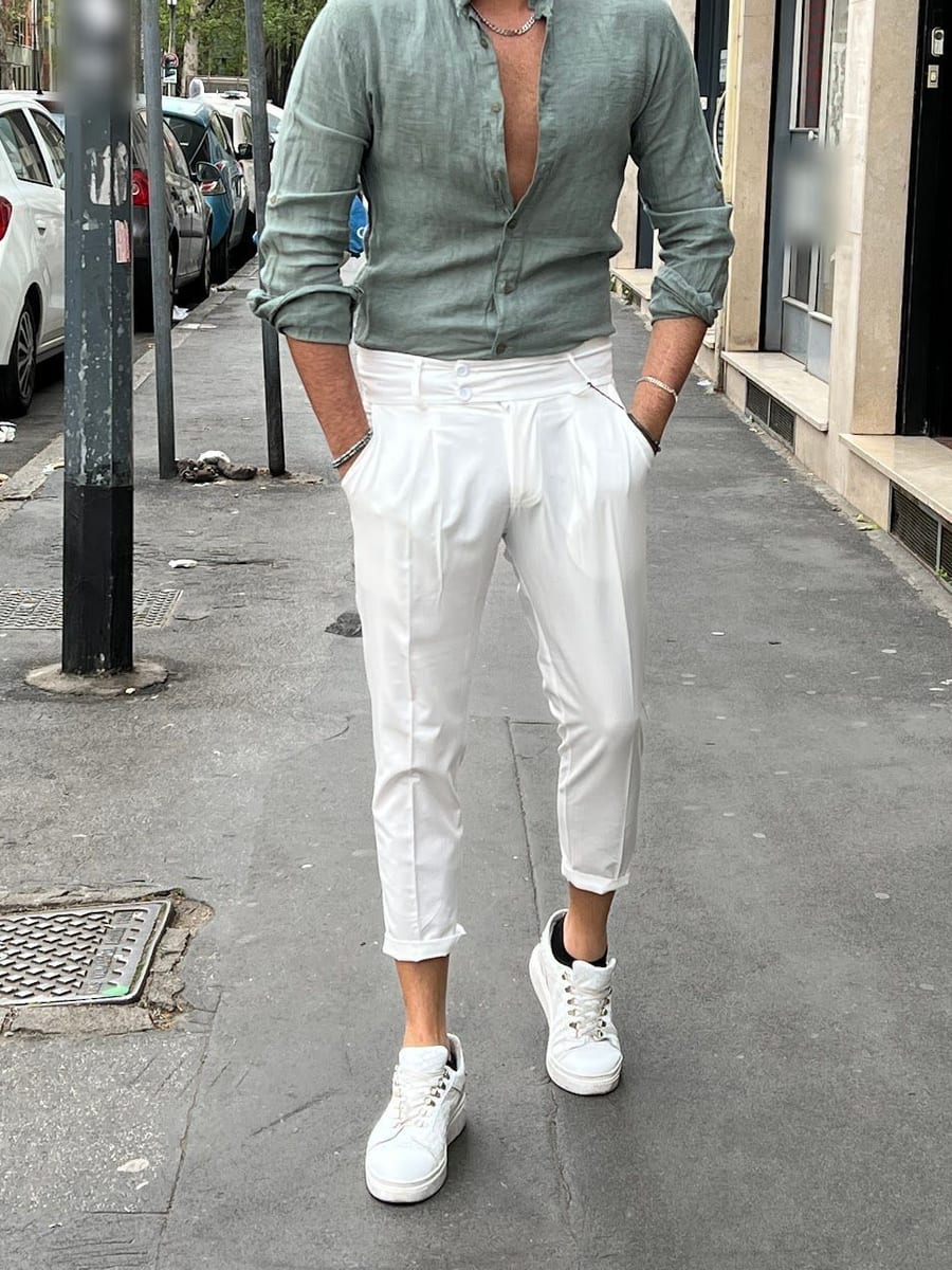 Look 01: camicia verde salvia con il collo alla coreana, pantalone bianco con le pinces e sneaker bianche, sul marciapiede davanti al negozio