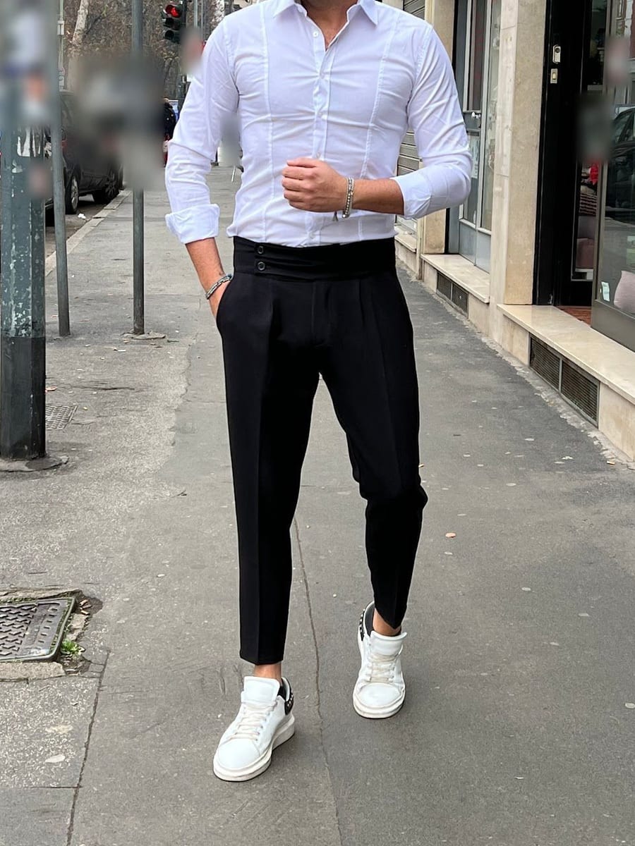 Look 03: camicia bianca, pantalone nero a vita alta con due bottoni e sneaker bianche, sul marciapiede davanti al negozio