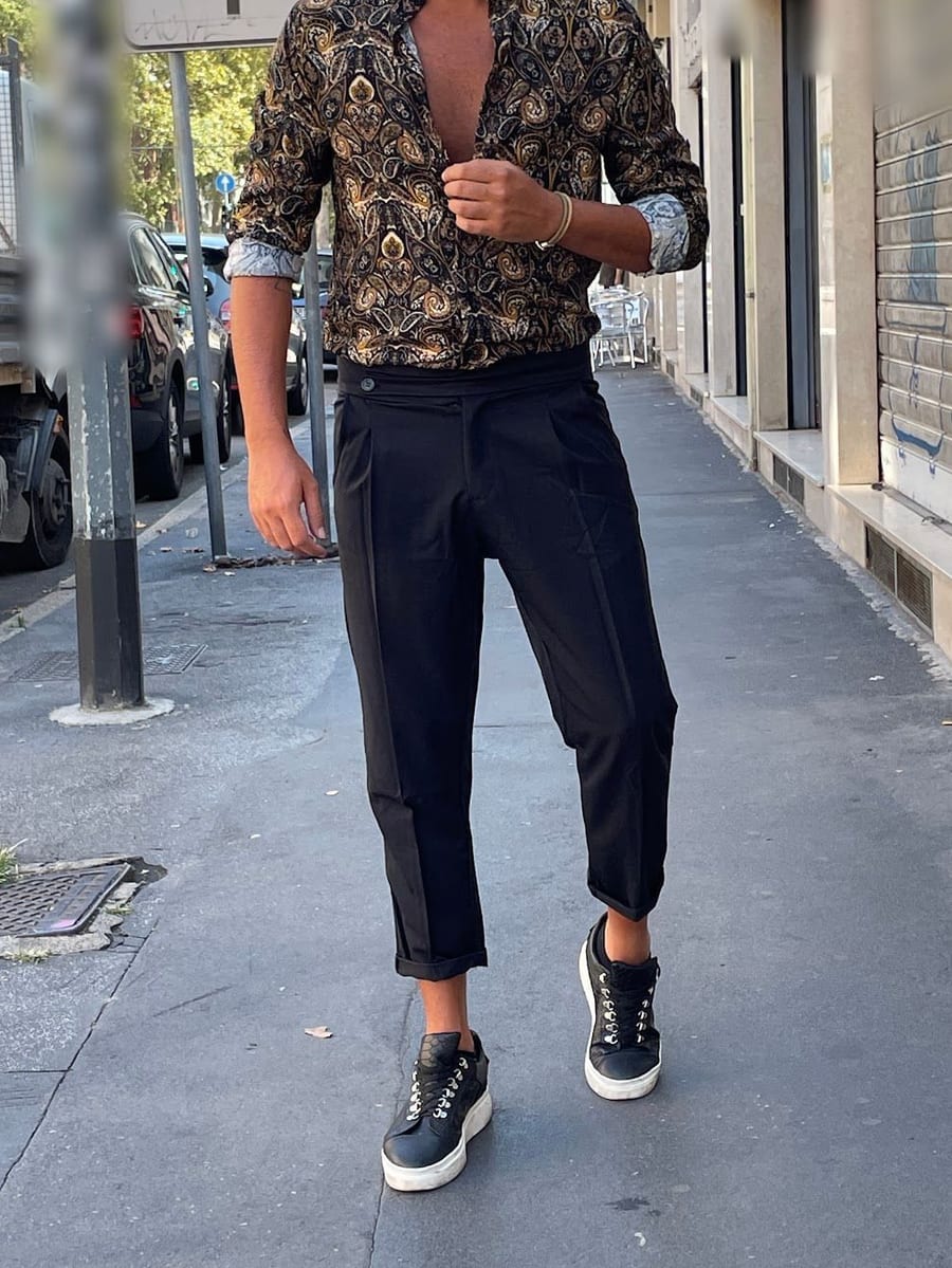 Look 05: camicia stampata oro e nero, pantalone blu scuro con la piega e sneaker nere, sul marciapiede davanti al negozio