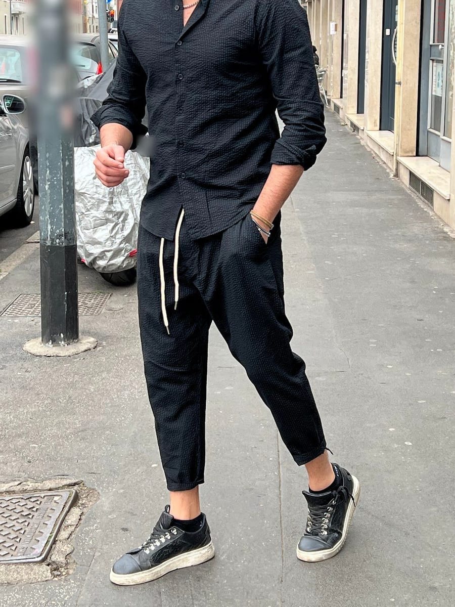 Look 08: camicia nera, pantalone nero con la coulisse bianca e sneaker nere, sul marciapiede