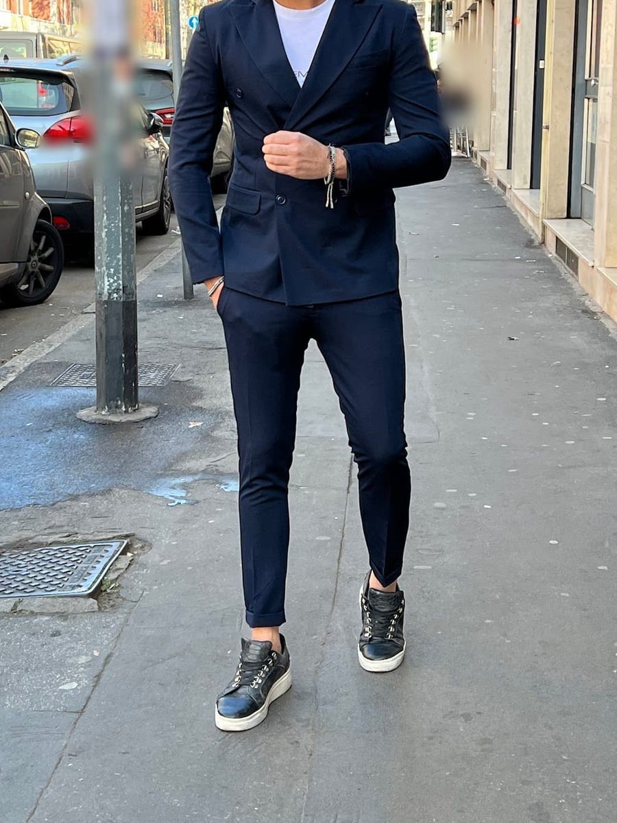 Look 10: completo doppiopetto blu con t-shirt bianca e sneaker nere, sul marciapiede davanti al negozio