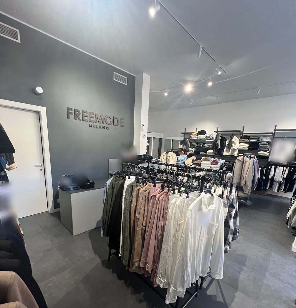 Dentro il negozio: la parete grigia con la scritta FREEMODE MILANO in rilievo e uno stender di camicie