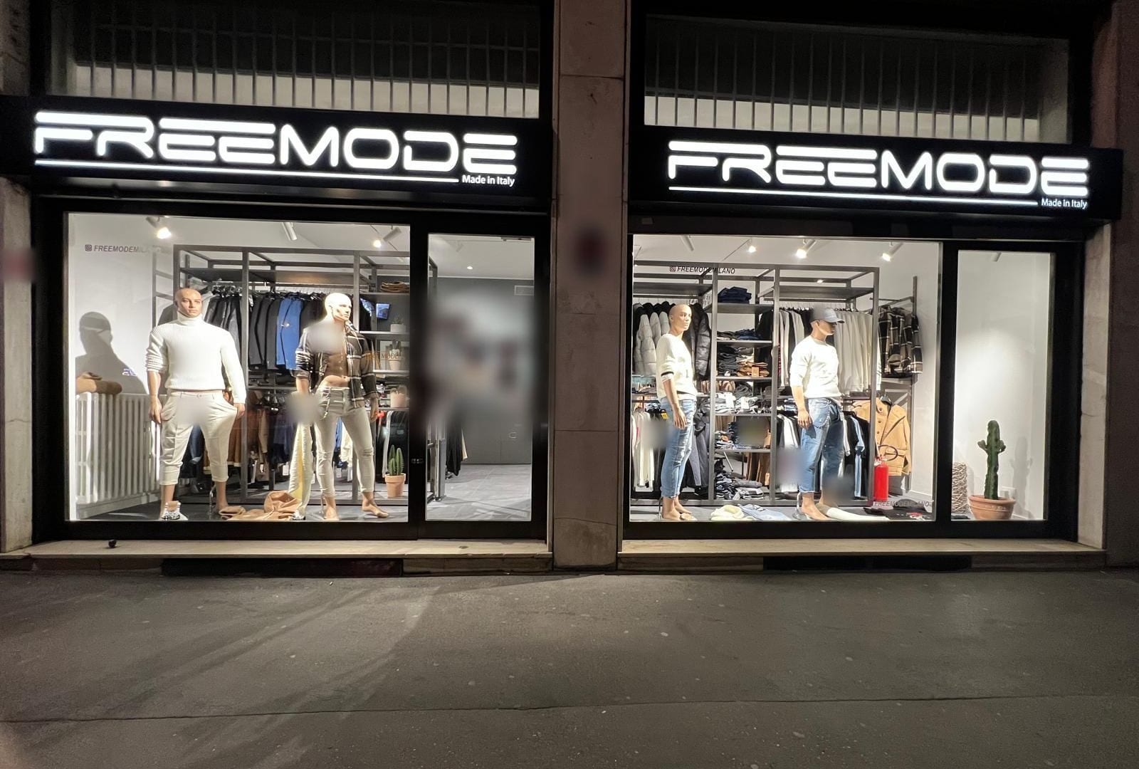 Le due vetrine di Freemode in Via Giambellino 79, la sera, con le insegne FREEMODE accese e i manichini