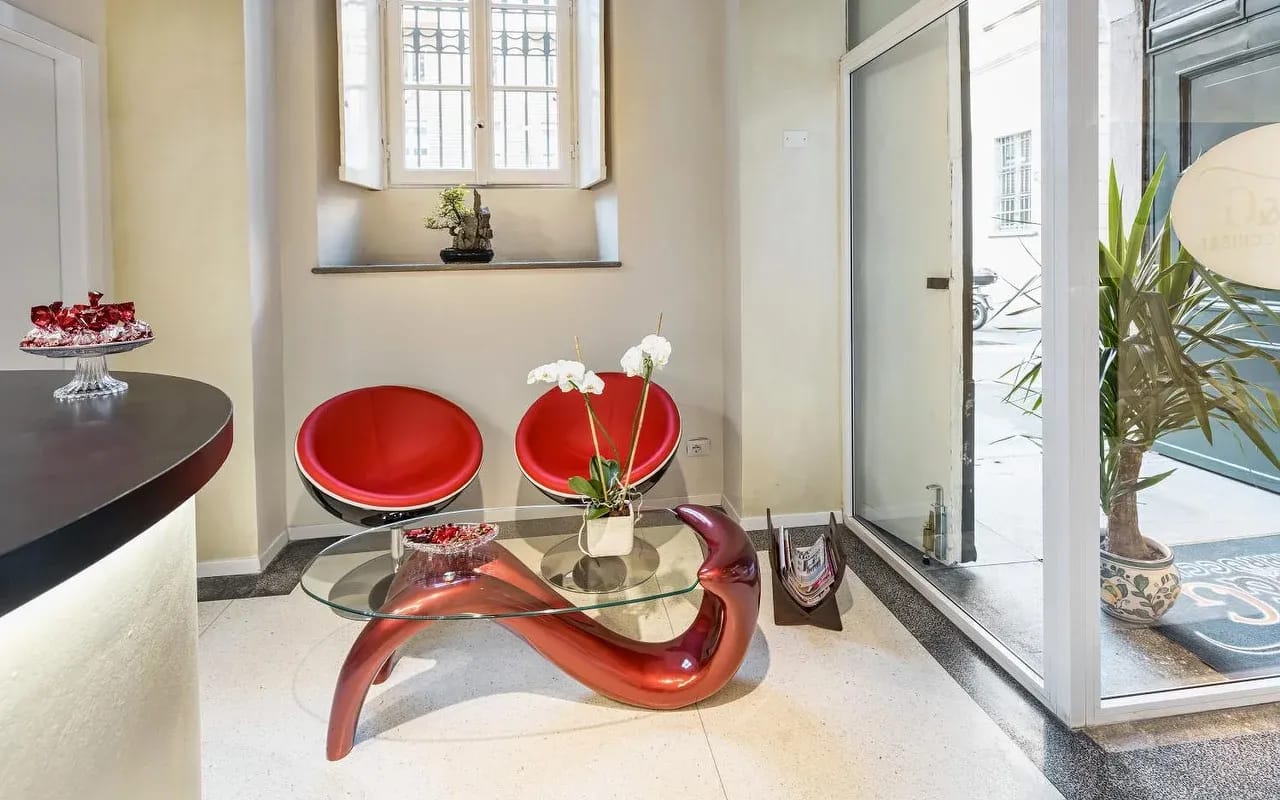 L'attesa: le poltroncine rosse e il tavolino rosso, la finestra col bonsai, l'insegna ovale sulla porta.