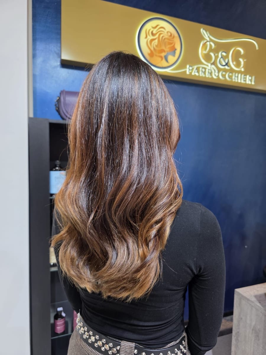 Un balayage castano e caramello, di spalle, davanti alla nostra insegna.