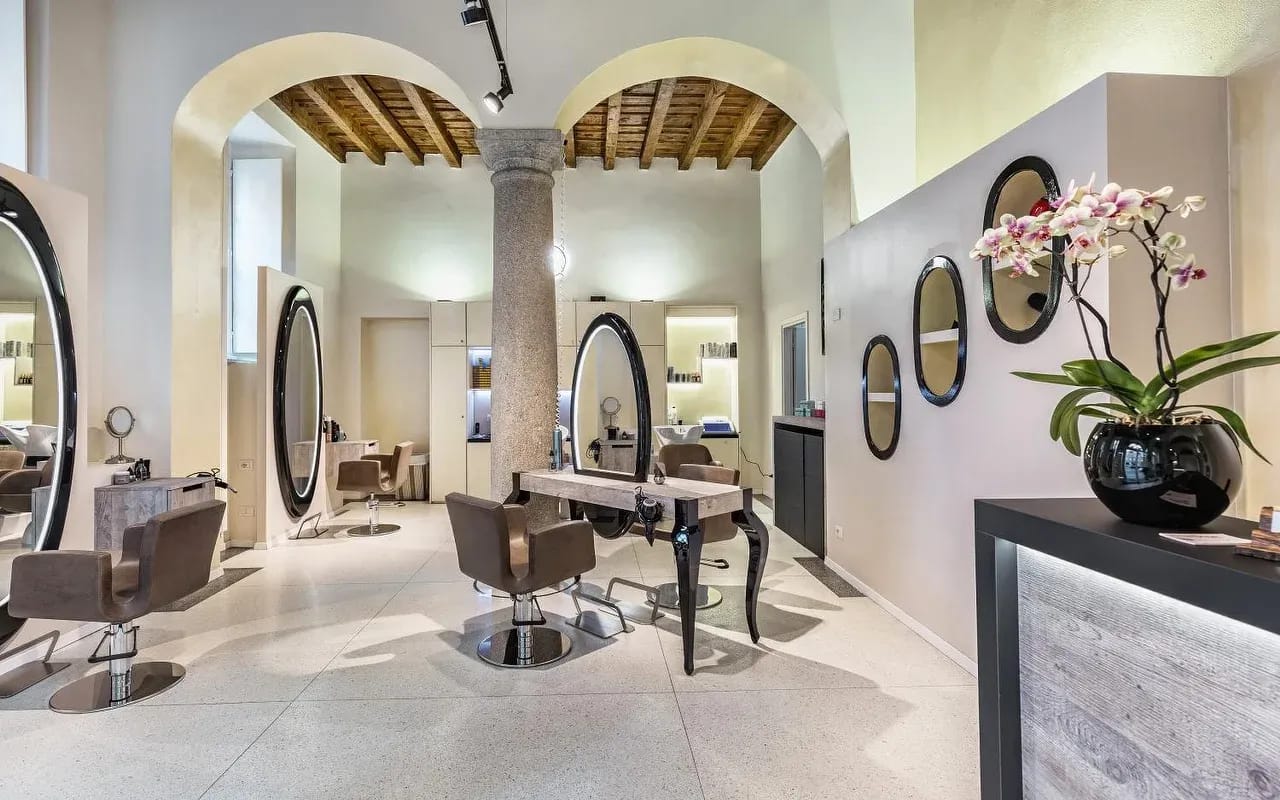 Il salone: i due archi, la colonna di granito, il soffitto a travi, le postazioni con gli specchi ovali.