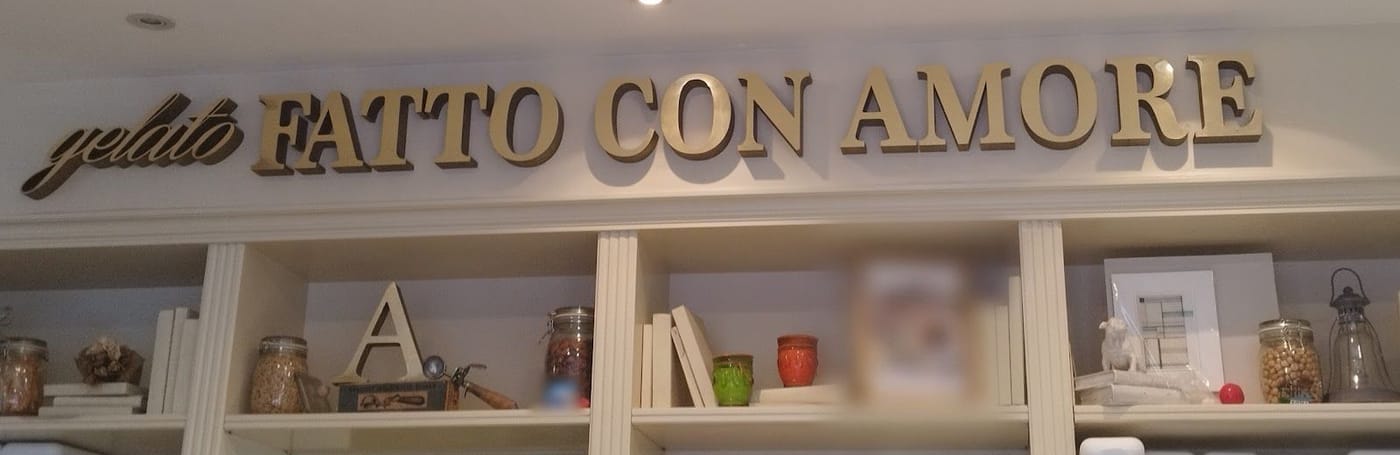 La scritta dorata «gelato FATTO CON AMORE» sopra le mensole, con la A, i barattoli e le coppette.
