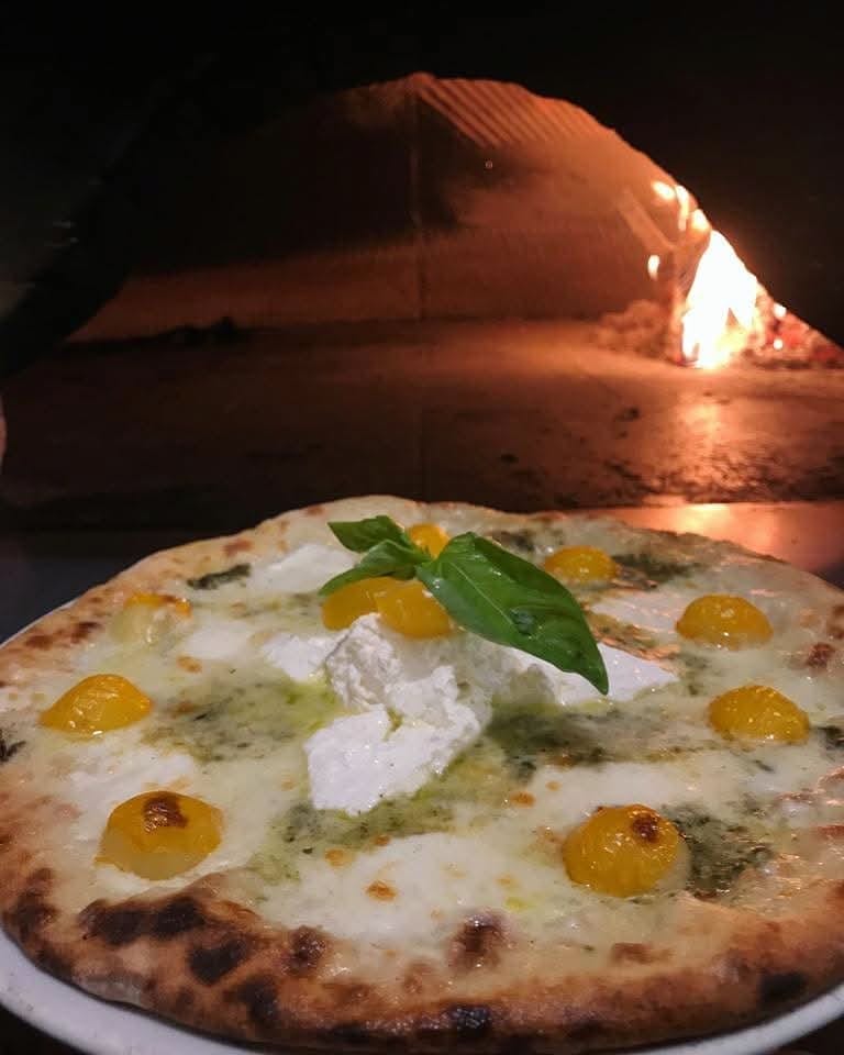 Pizza appena sfornata davanti alla bocca del forno a legna acceso