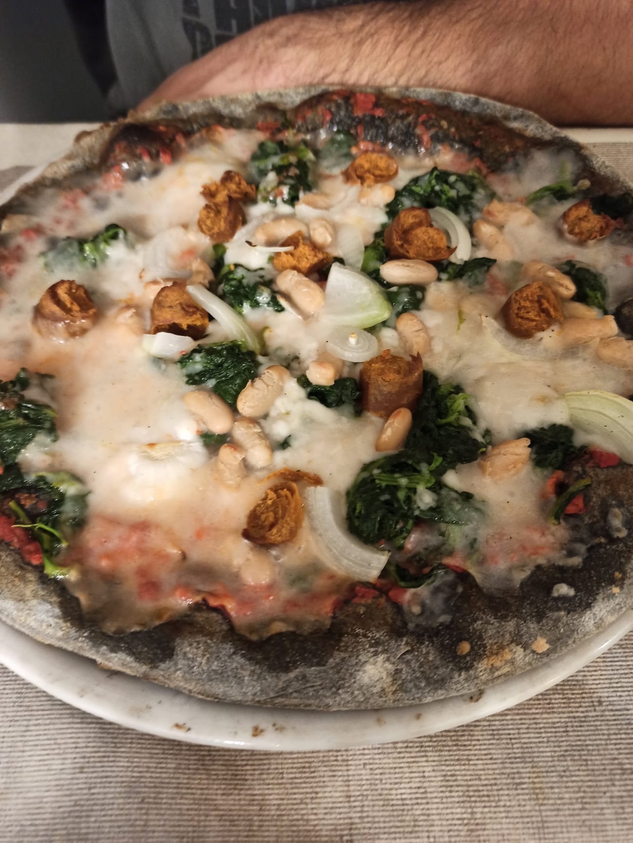 Pizza con impasto scuro al carbone vegetale, condita con verdure, fagioli e mozzarella vegetale