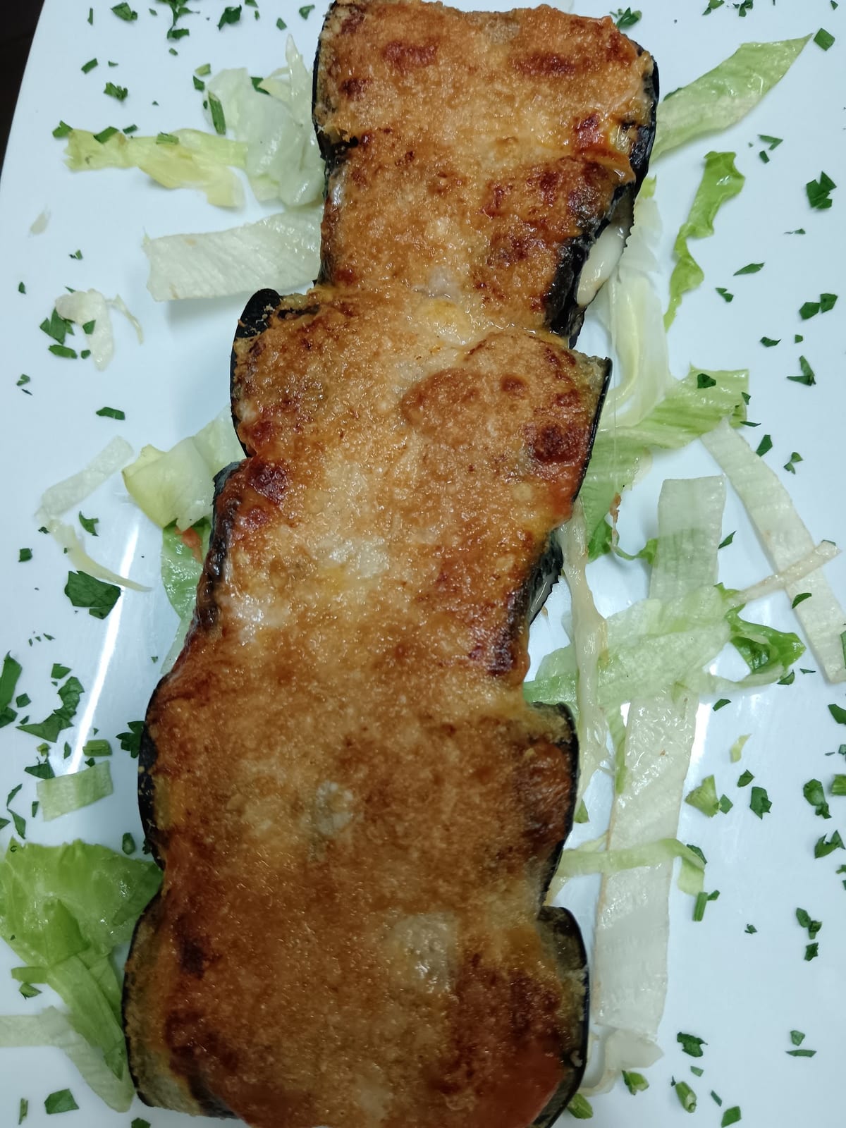 Involtini di melanzane gratinati serviti su piatto bianco