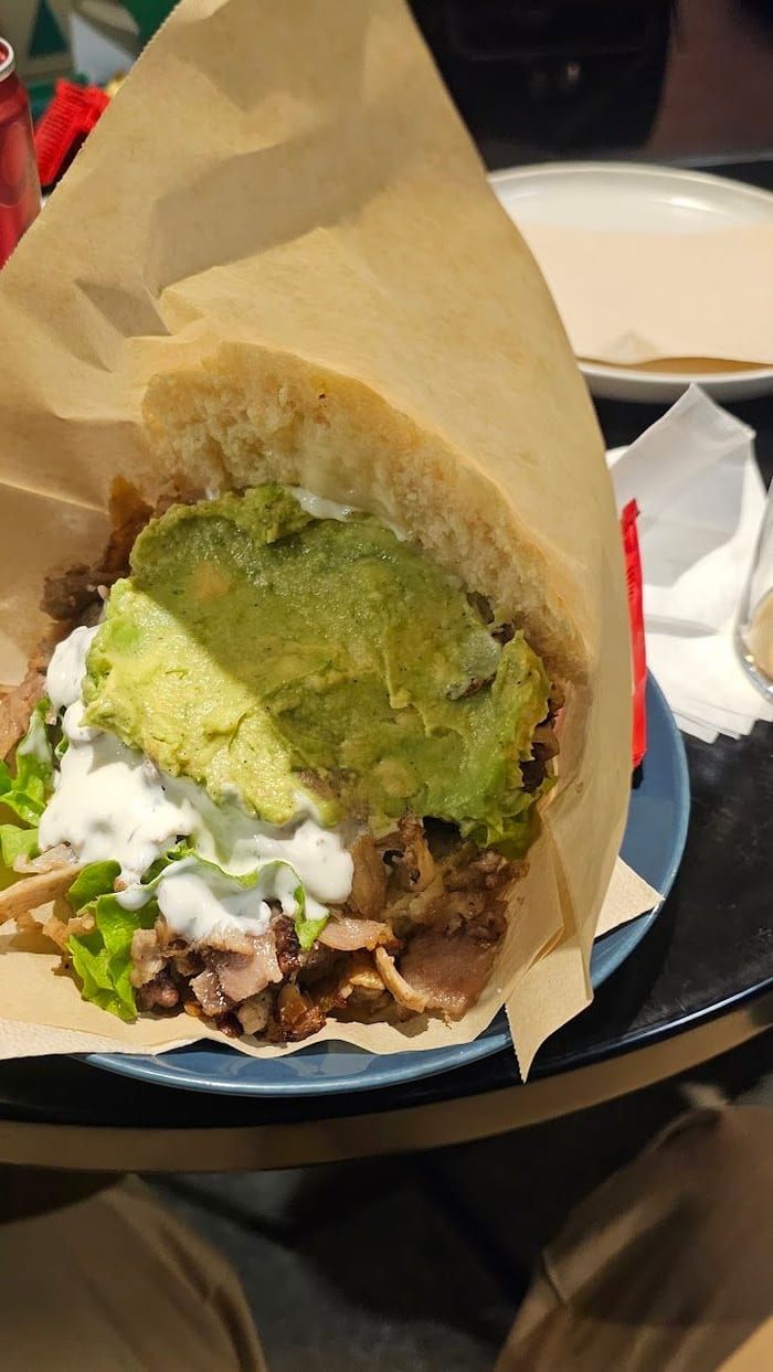 Un panino nella carta a cono, con la carne, la salsa bianca, l'insalata e l'avocado.
