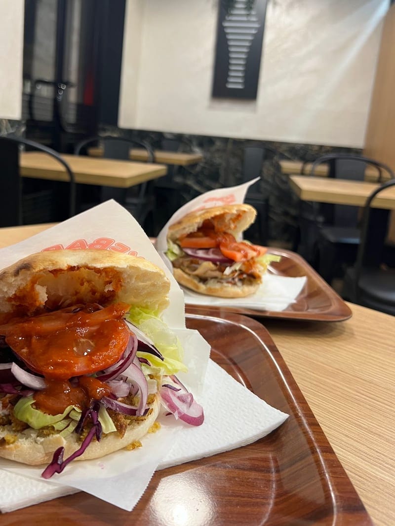 Due panini kebap sui vassoi, con la salsa rossa, il cavolo viola e l'insalata.