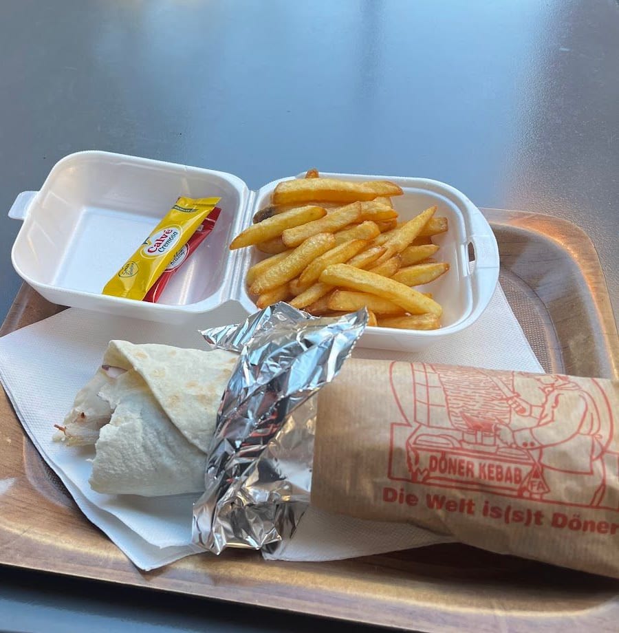 Una piadina arrotolata nella stagnola, le patatine e una bustina di salsa su un vassoio, a un tavolo fuori.