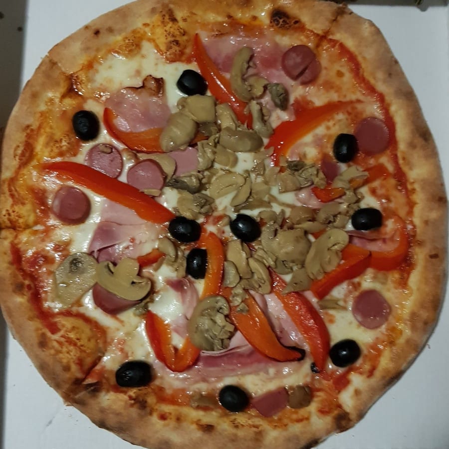 Una pizza vista dall'alto con prosciutto, funghi, peperoni, olive e würstel.