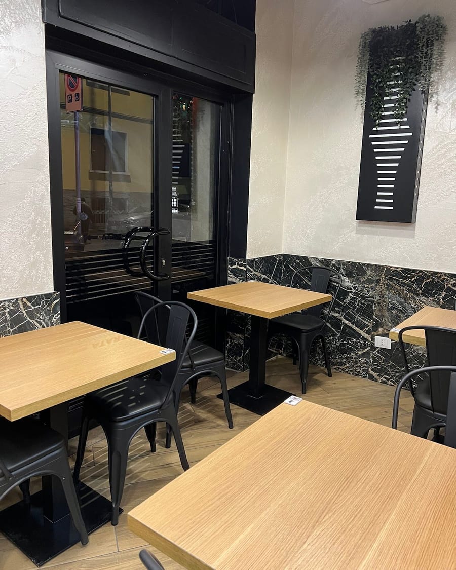 La sala: tavoli di legno chiaro, sedie nere di metallo, il marmo nero alle pareti e un pannello a righe.