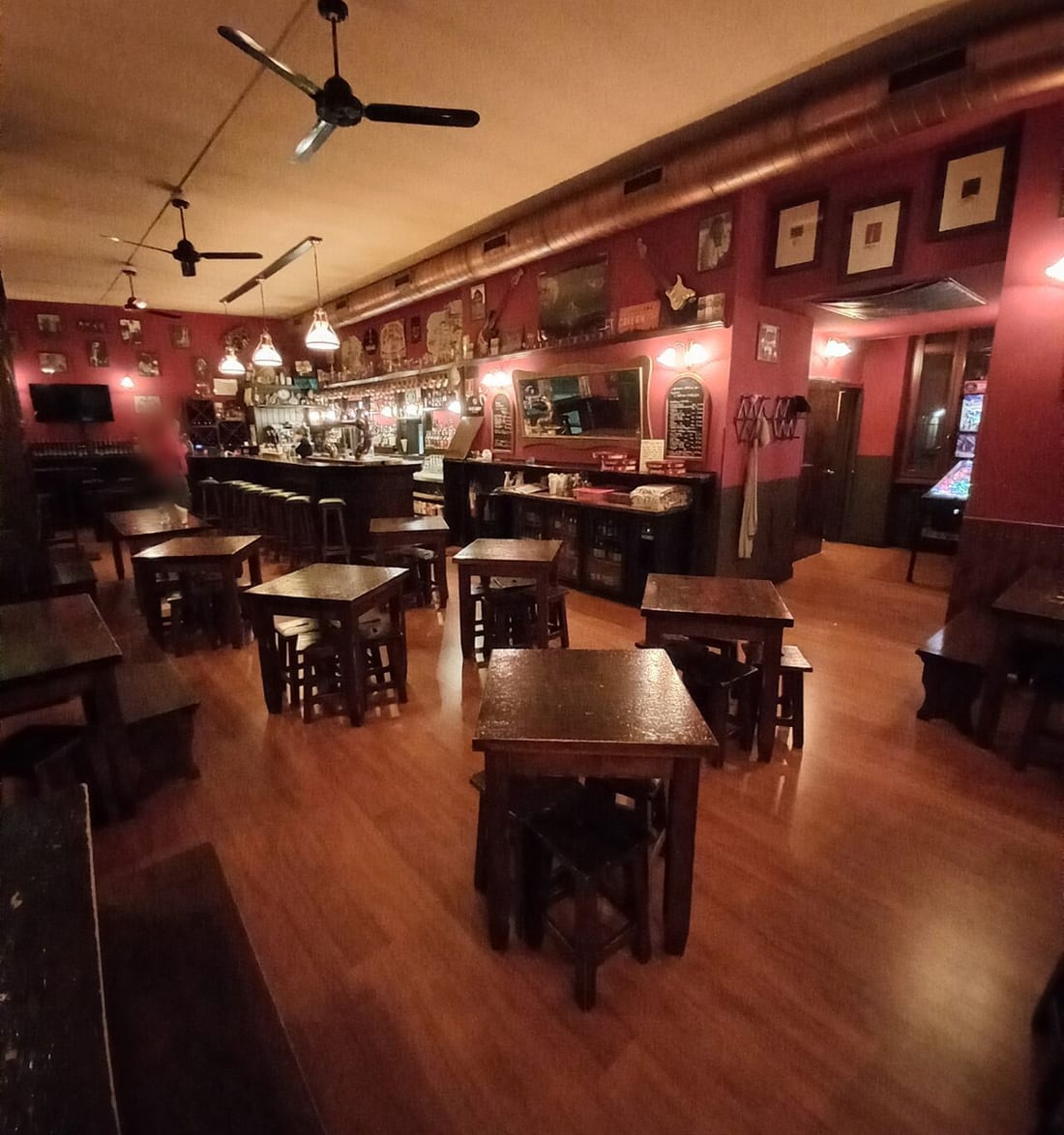 La sala coi tavoli di legno scuro, le pareti rosse coi quadri e il bancone in fondo