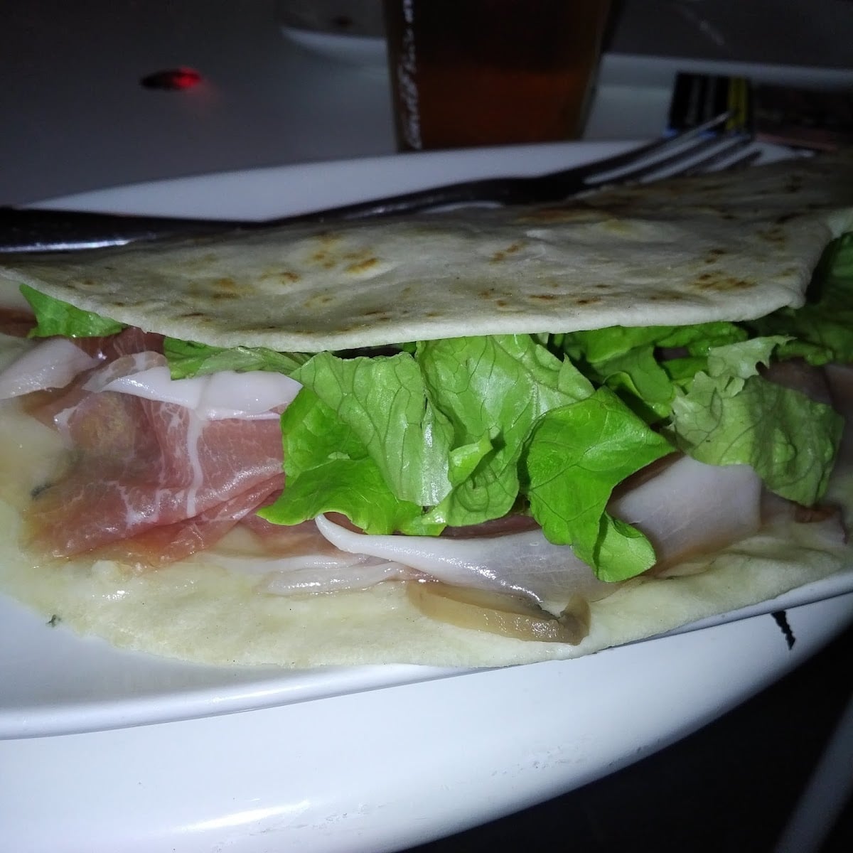 Una piadina farcita con prosciutto crudo, prosciutto cotto e insalata, aperta su un piatto bianco