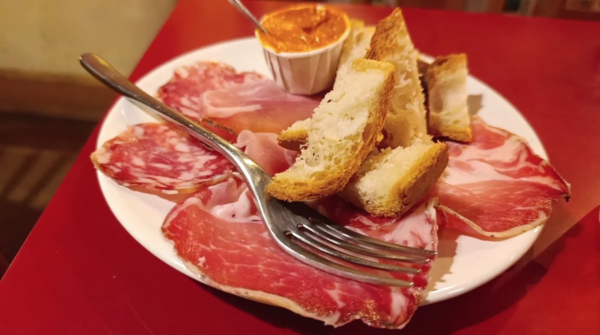 Un piatto di salumi affettati con crostini di pane e una salsa, su un tavolo rosso