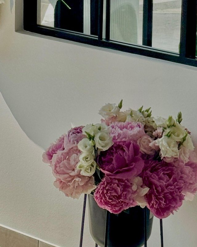 Un vaso di peonie rosa davanti alla parete bianca del salone
