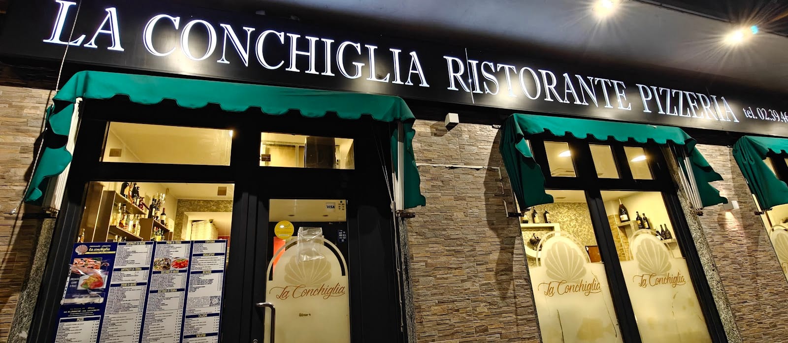 La facciata de La Conchiglia di sera, con l'insegna Ristorante Pizzeria e il logo a conchiglia