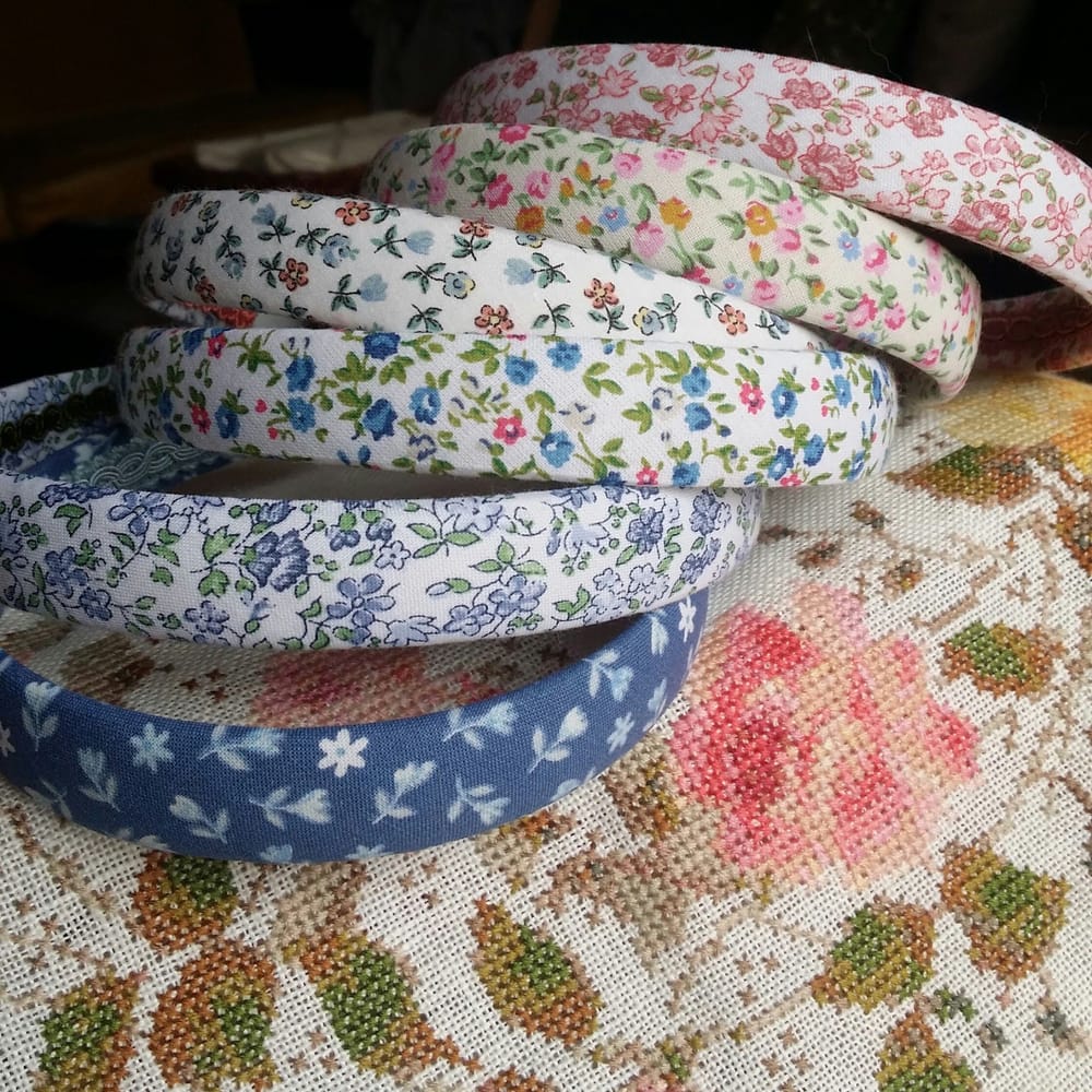 Cerchietti rivestiti di stoffa a fiorellini, appoggiati su un ricamo a punto croce con una rosa.