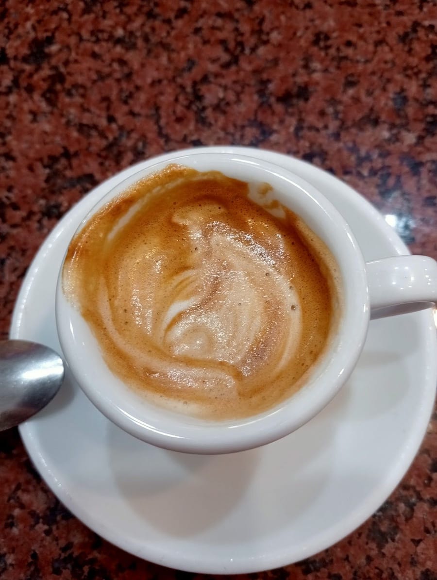 Un cappuccino visto dall'alto, sul bancone di granito rosso, col cucchiaino sul piattino