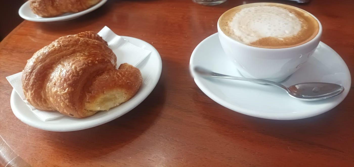 Un cappuccino col cuore e due brioche sul tavolino di legno