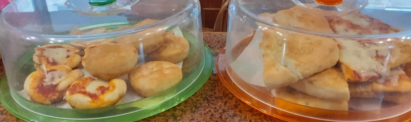 Pizzette e torte salate sotto due campane di plastica, una verde e una arancione