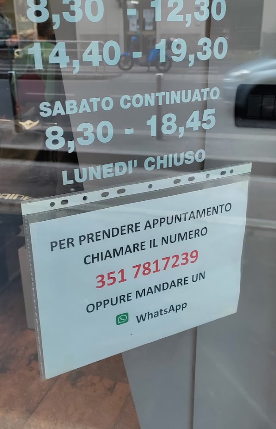 Il cartello sulla vetrina: per prendere appuntamento chiamare il numero oppure mandare un WhatsApp