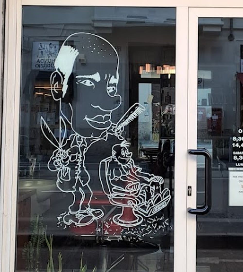Il disegno sul vetro: un barbiere con pettine e forbici che taglia i capelli a un bambino
