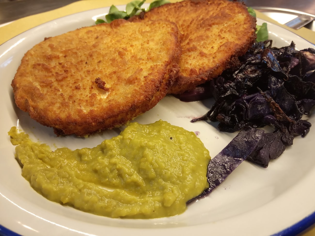 Cotolette impanate con purè di piselli e cavolo viola brasato, nel piatto col bordo blu