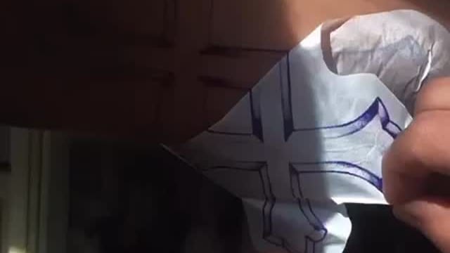 Due mani staccano la carta dello stencil dalla pelle: resta il disegno viola di una croce.