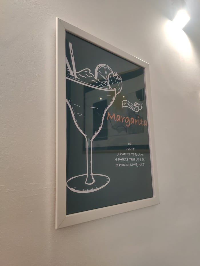 Una stampa appesa in sala: il disegno bianco di un Margarita su fondo verde scuro.