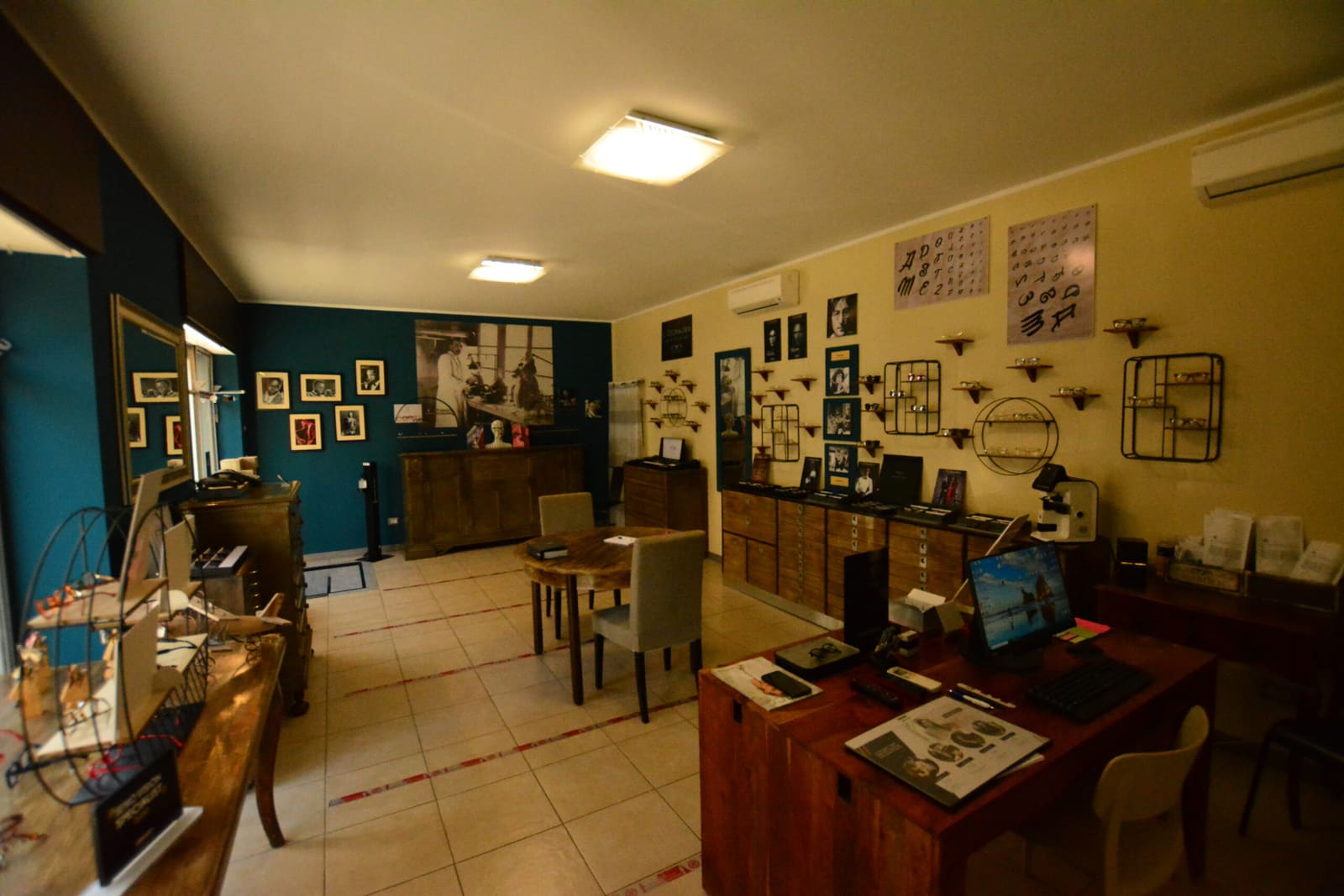 L'interno del negozio: pareti petrolio, mobili di legno chiaro e le foto d'epoca degli ottici al lavoro